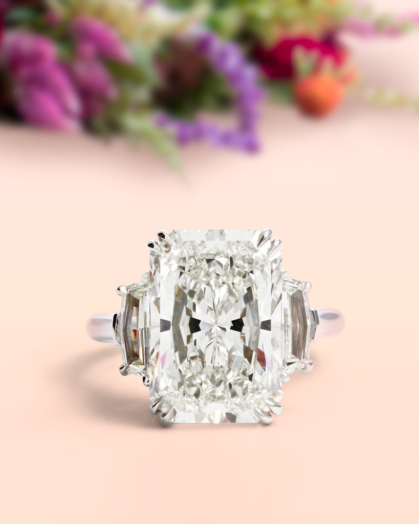 Huge radiant engagement ring on table with flowers in the background. 