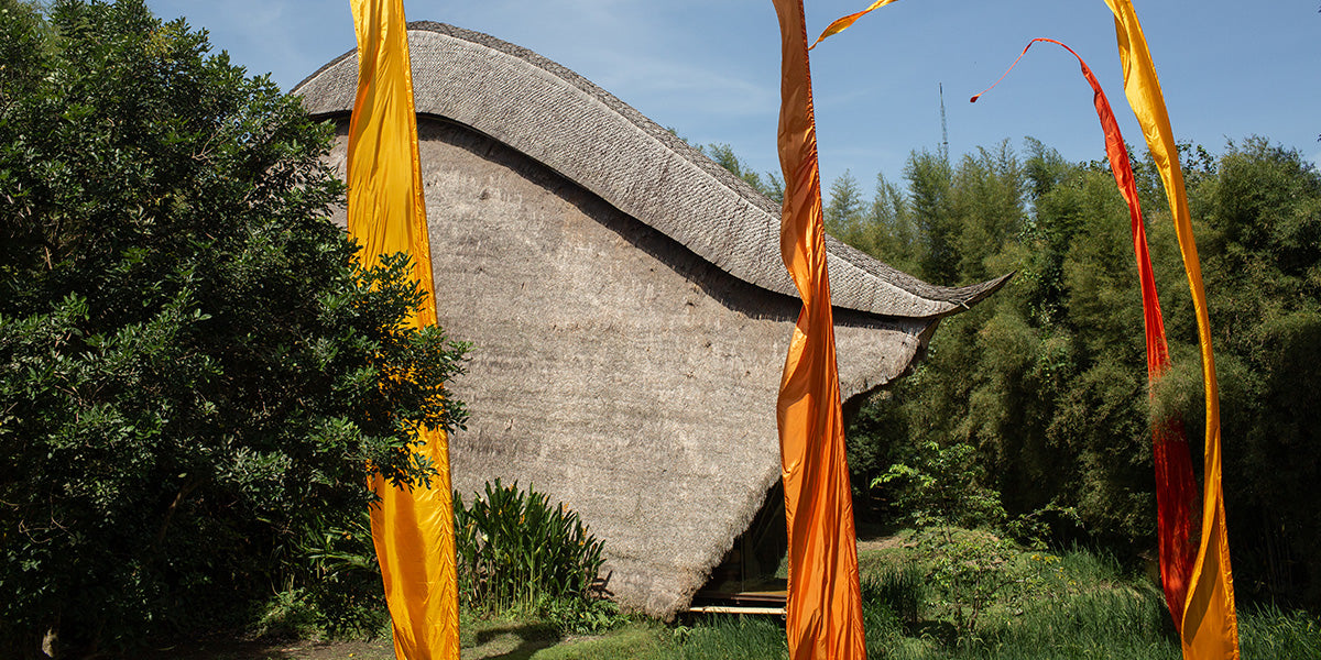 John Hardy's open-air workshop in Bali, with a sweeping thatched roof framed by orange ceremonial flags