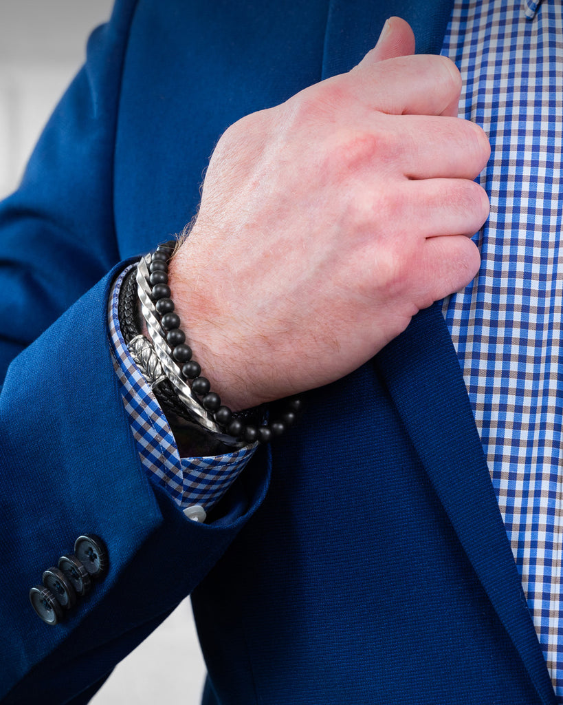 Gentleman wearing bracelets holding his suit lapel. 
